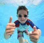 A young boy is swimming underwater in a pool and giving a thumbs up.