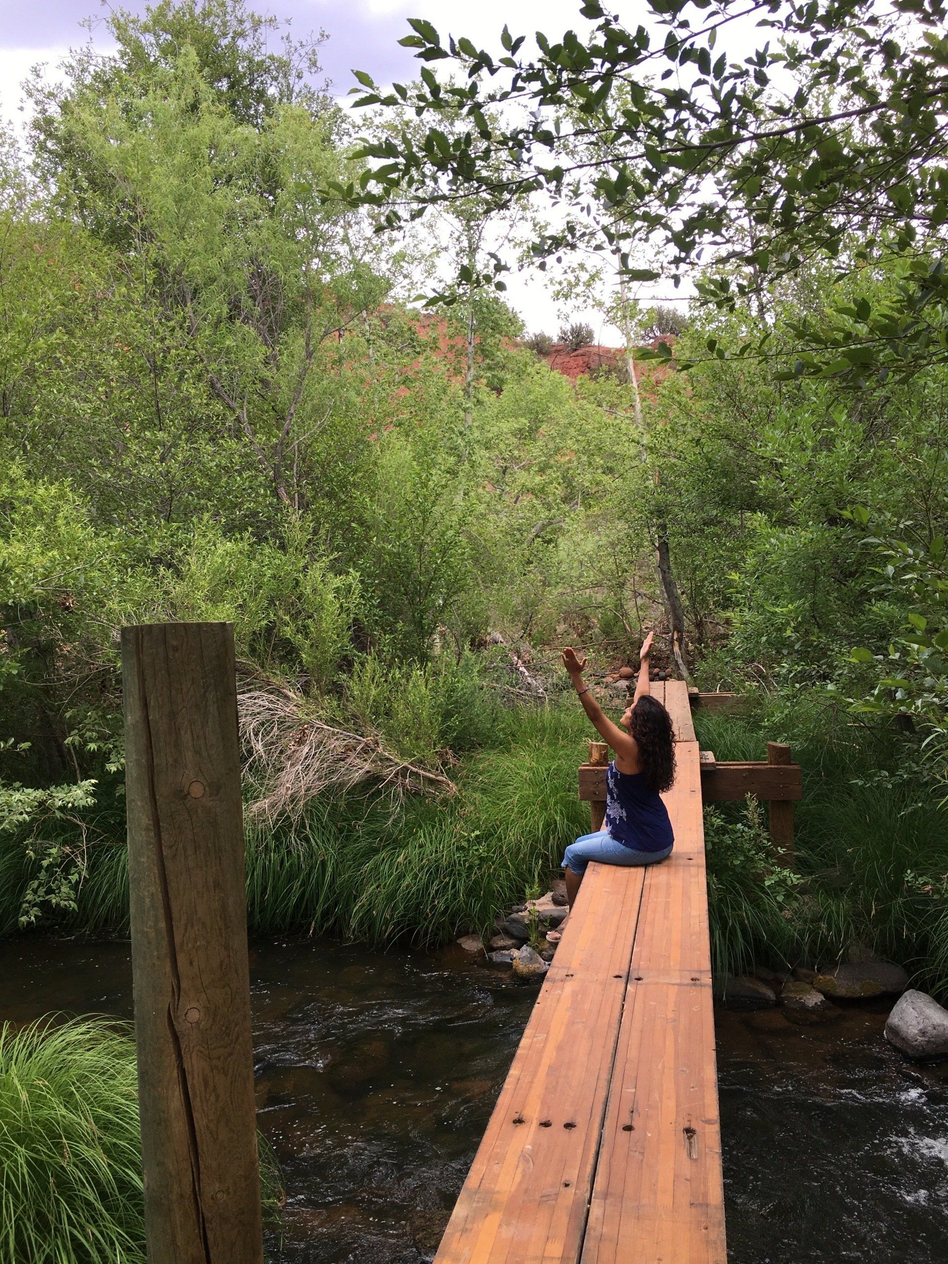 A woman is sitting on a wooden bridge over a river.