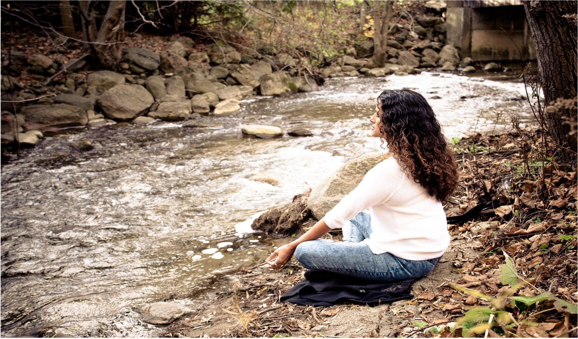 A woman is sitting by a stream looking at the water