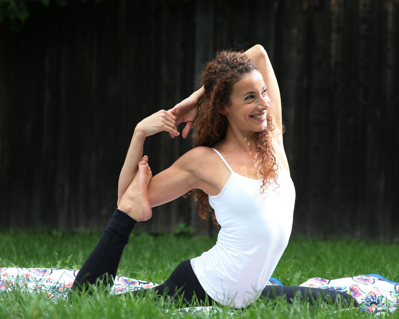 A woman is sitting on a yoga mat in the grass.