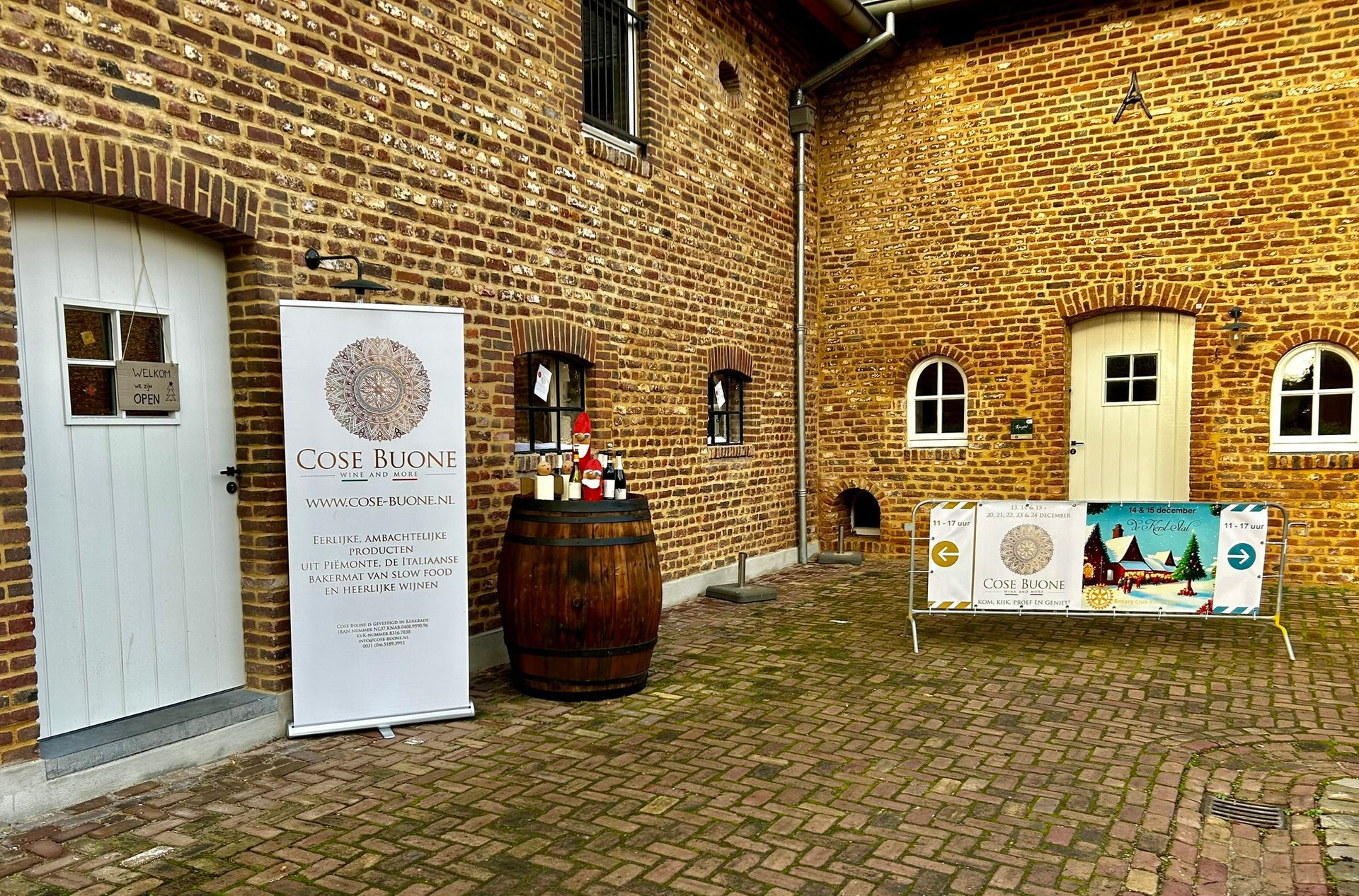 De buitenkant van het gebouw is opgetrokken uit baksteen en heeft witte deuren, vlaggen, een wijnvat en kleine boogvensters.