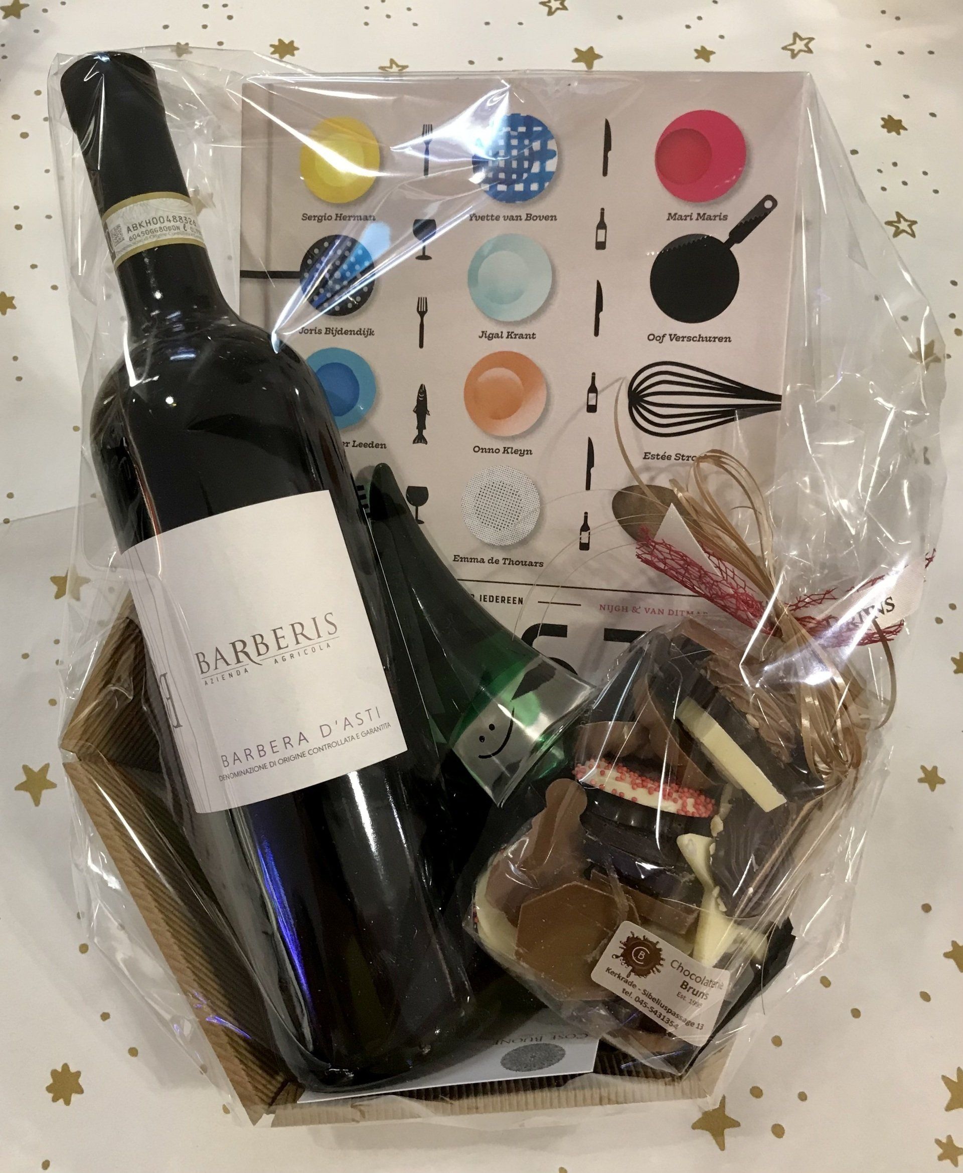 Cadeaupakket met een fles rode wijn, een klein flesje, lekkernijen en een kaartje met een keukenthema, verpakt in transparant cellofaan.