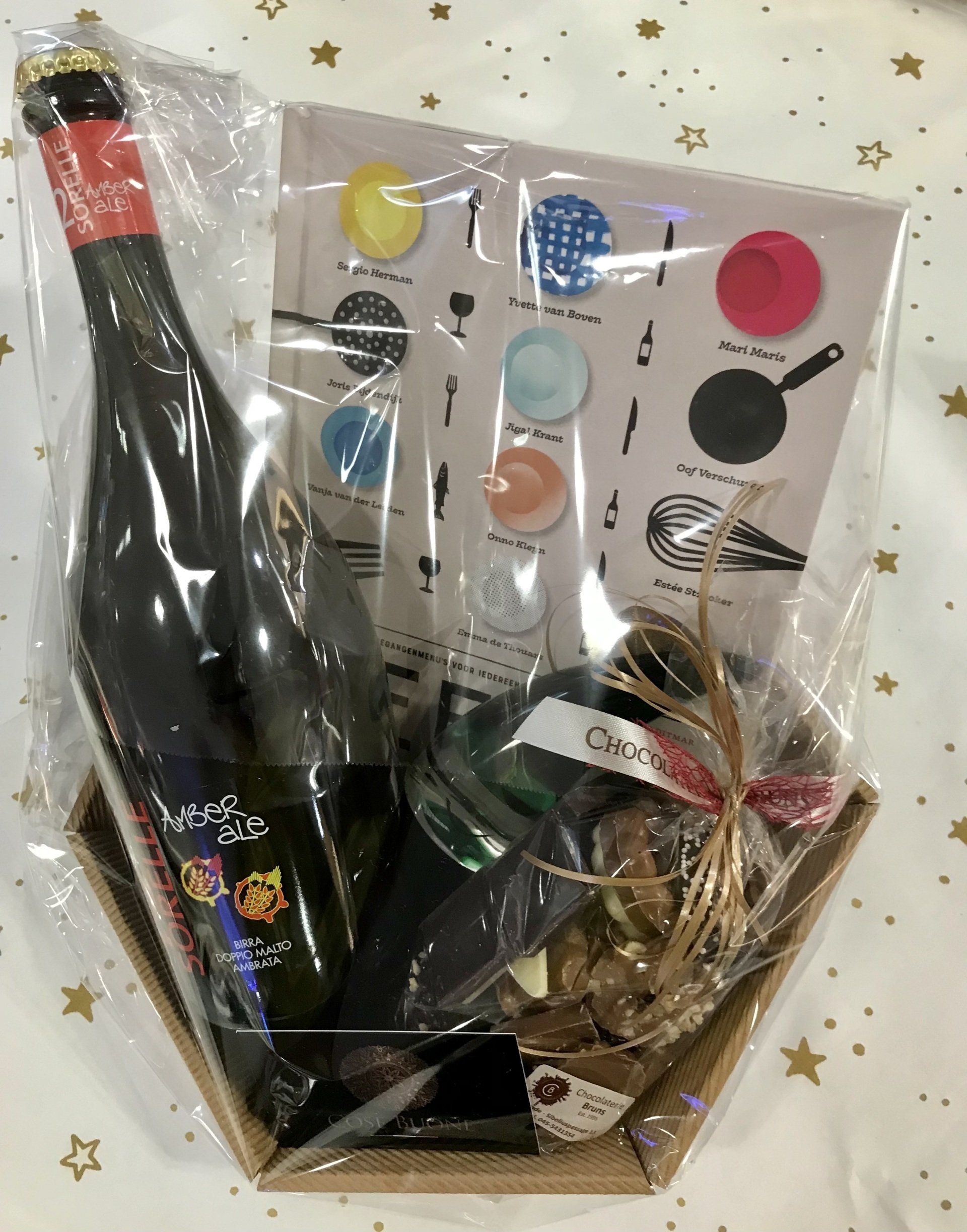 Cadeaupakket met een fles wijn, een pot en artikelen met een kookthema, verpakt in cellofaan.
