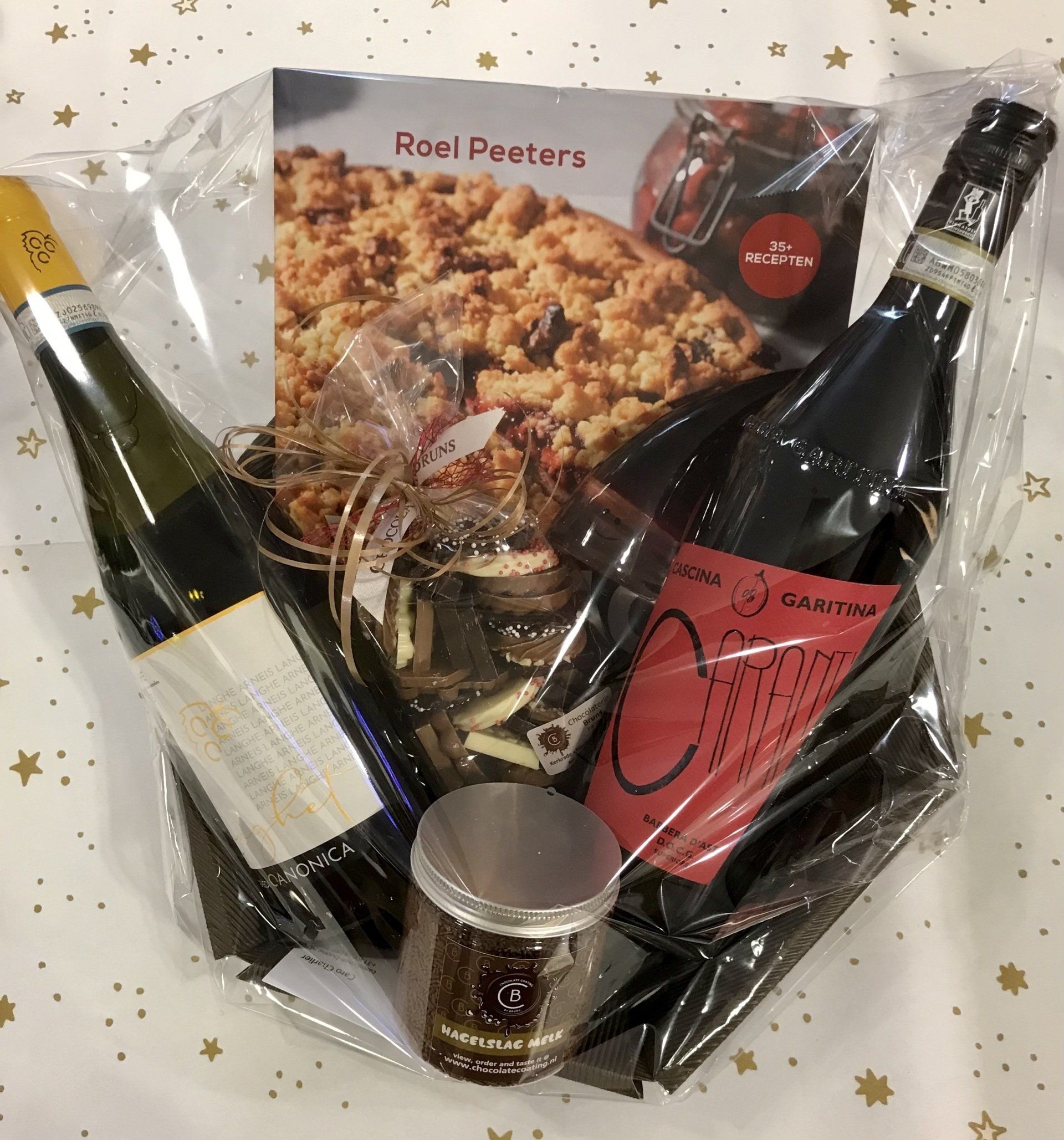 Cadeaupakket met wijnflessen, lekkernijen en een receptenboek, verpakt in transparant cellofaan.