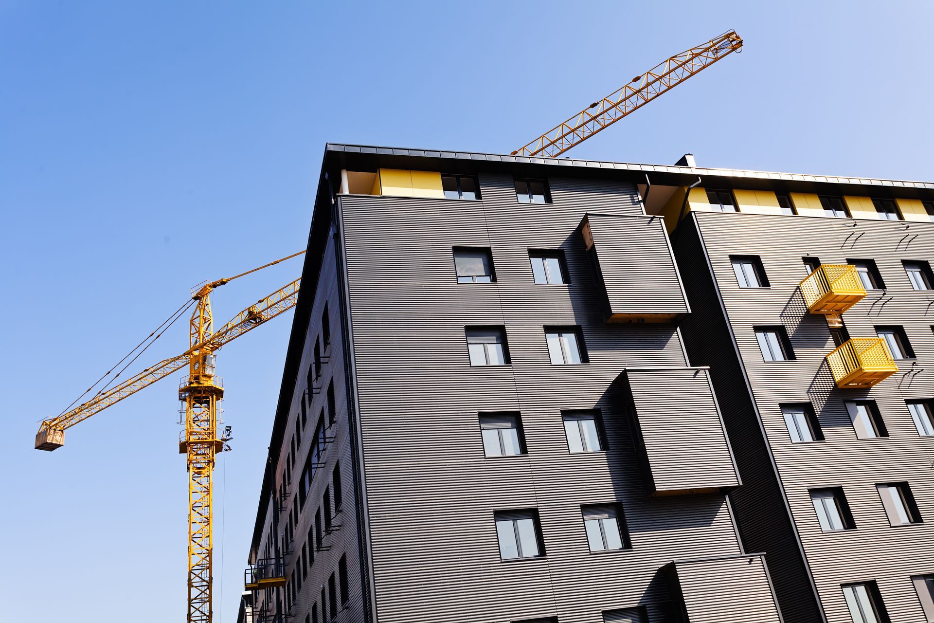 High-rise building under construction with two yellow cranes against a blue sky