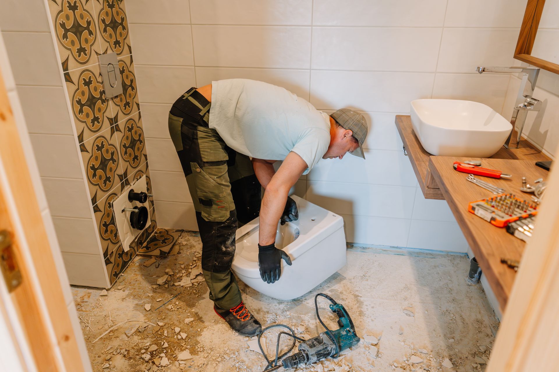 Worker installing a white toilet in a tiled bathroom with tools on the floor