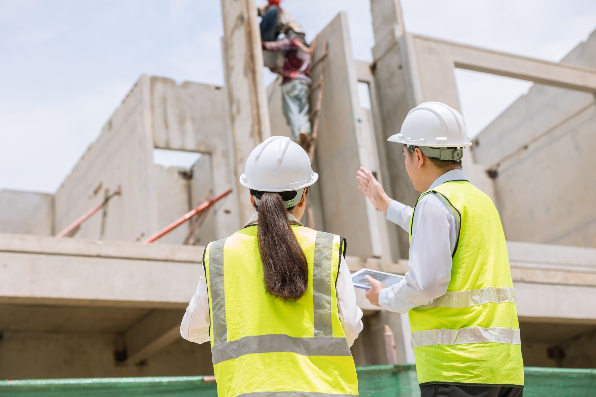 Two construction workers in hard hats and safety vests inspecting a concrete building site