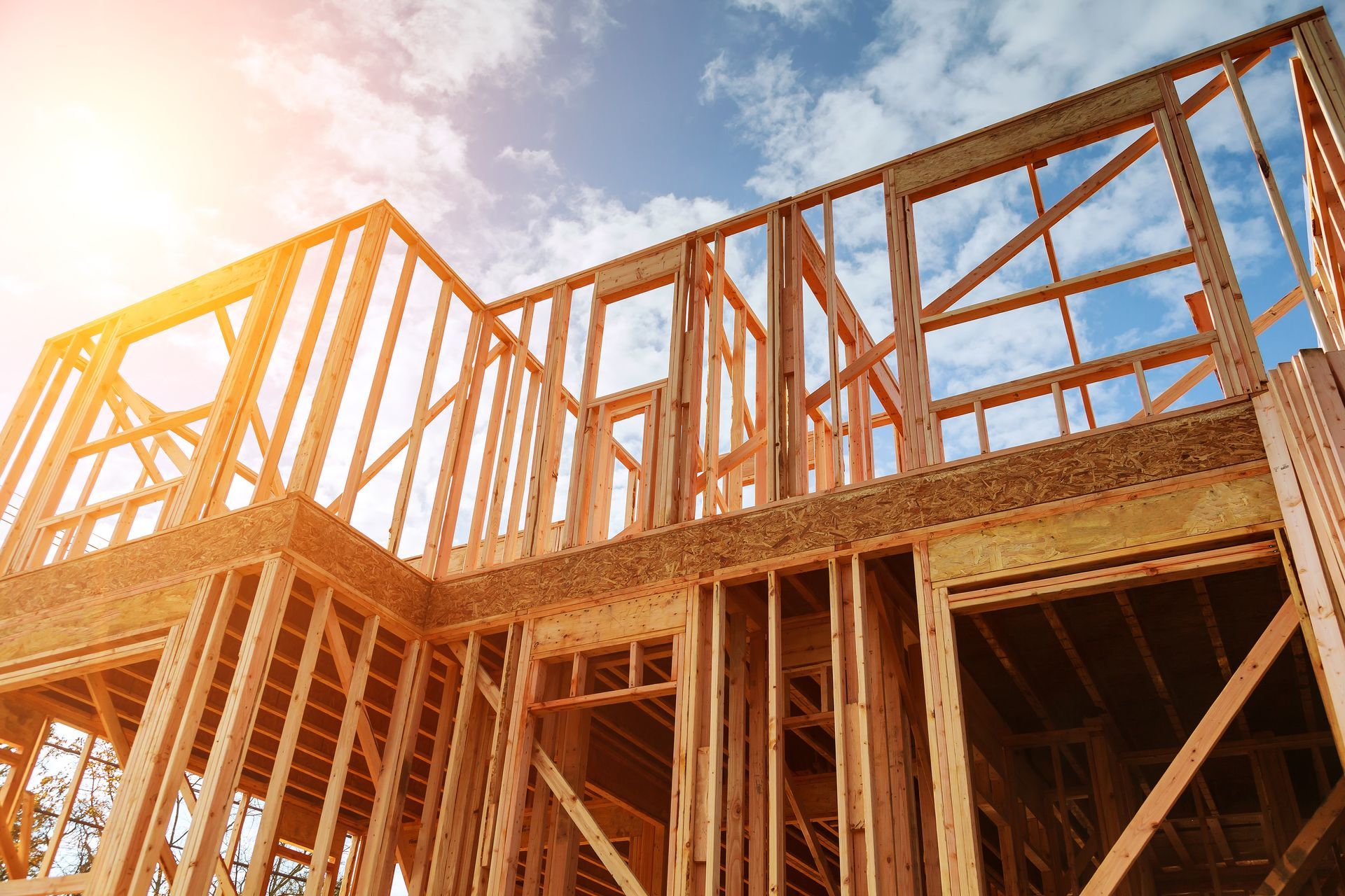 Wooden house framing under construction against a bright blue sky, seen from a low angle