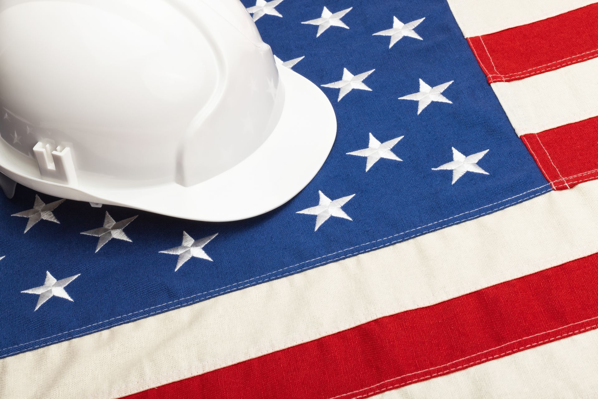 White hard hat on a folded U.S. flag background with stars and stripes.