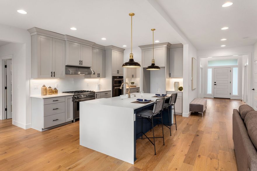 Bright modern kitchen with white cabinets, island, pendant lights, and hardwood floors, opening to a hallway