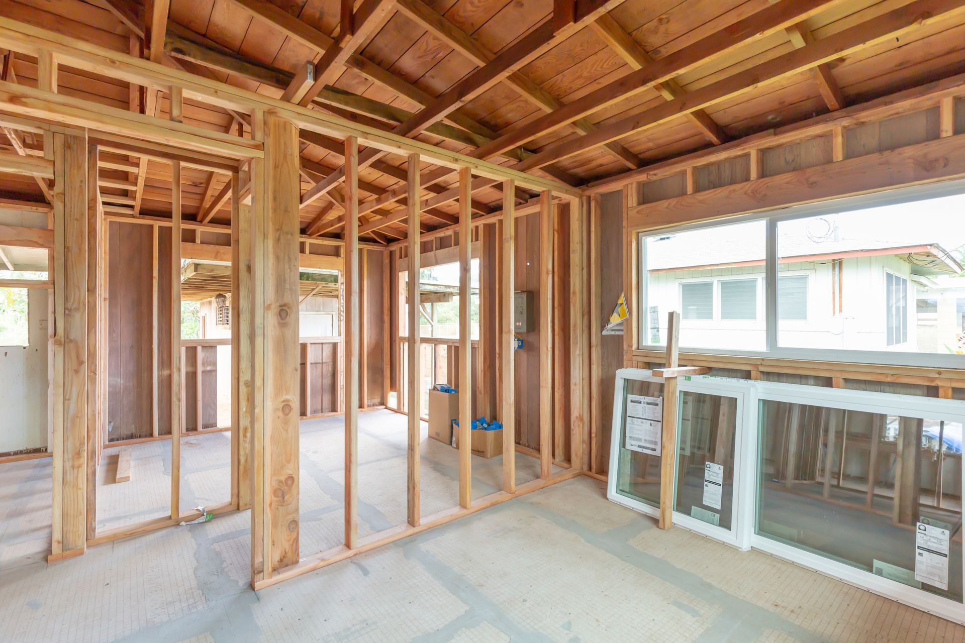 Unfinished wooden house interior with exposed framing, beams, and a window leaning against the wall.