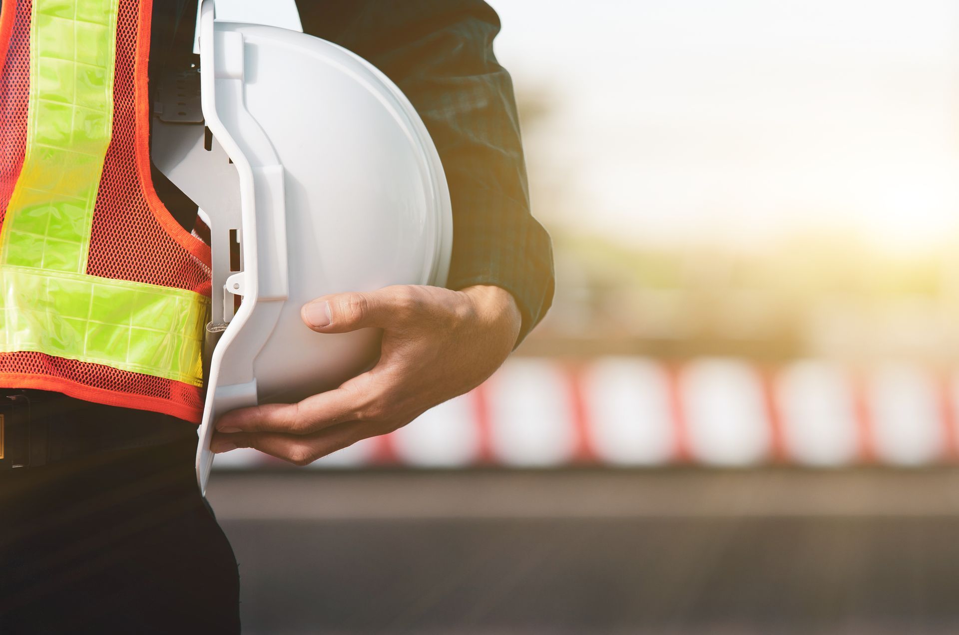 Construction worker holding a white hard hat beside a reflective safety vest outdoors