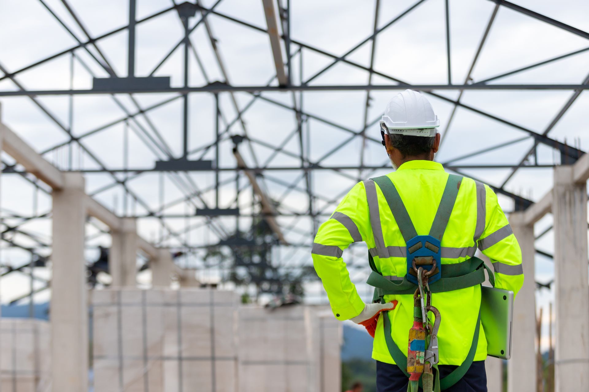 Construction worker in neon safety gear standing under steel framework at a building site