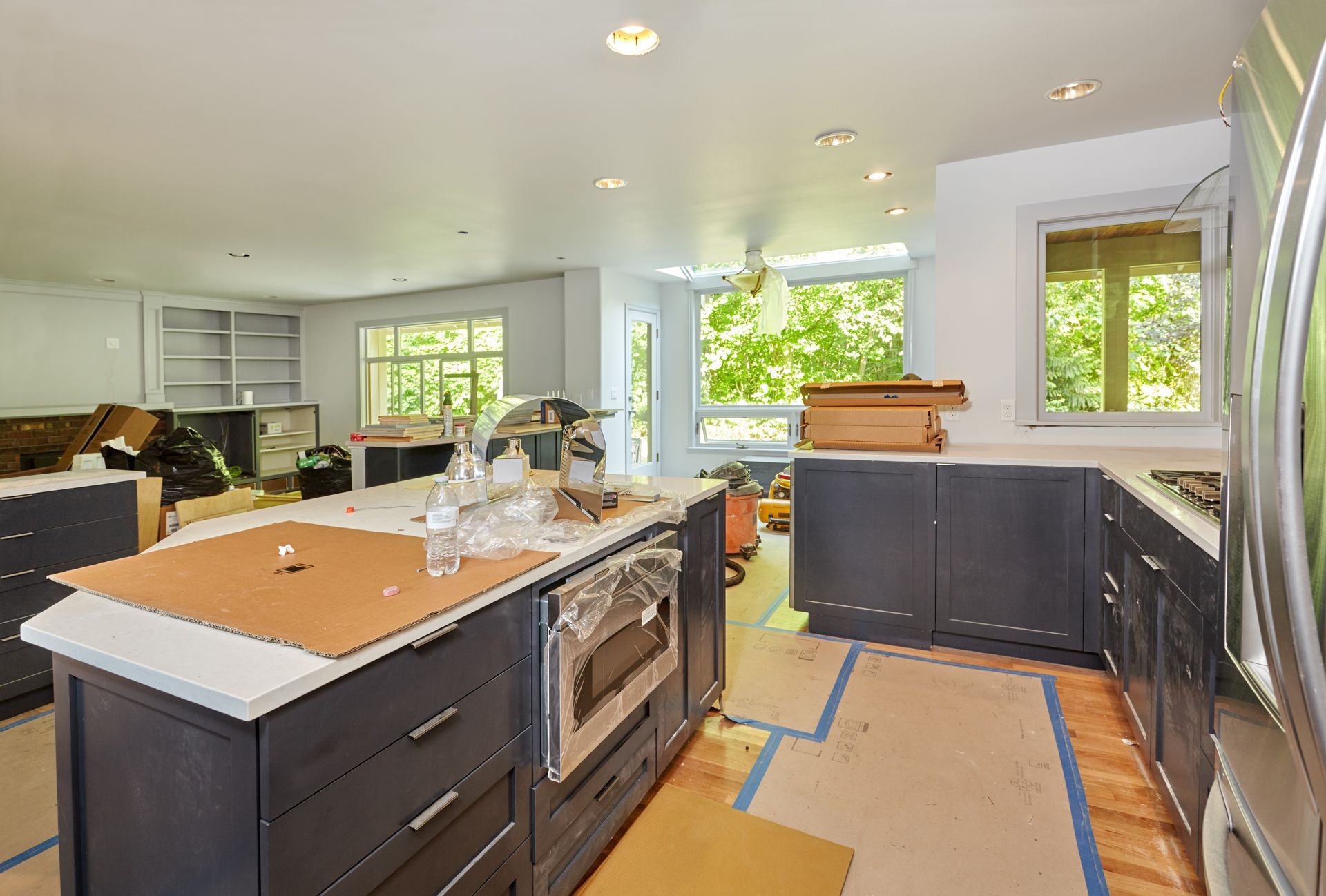 Bright kitchen under renovation with dark cabinets, island, and tools on the floor