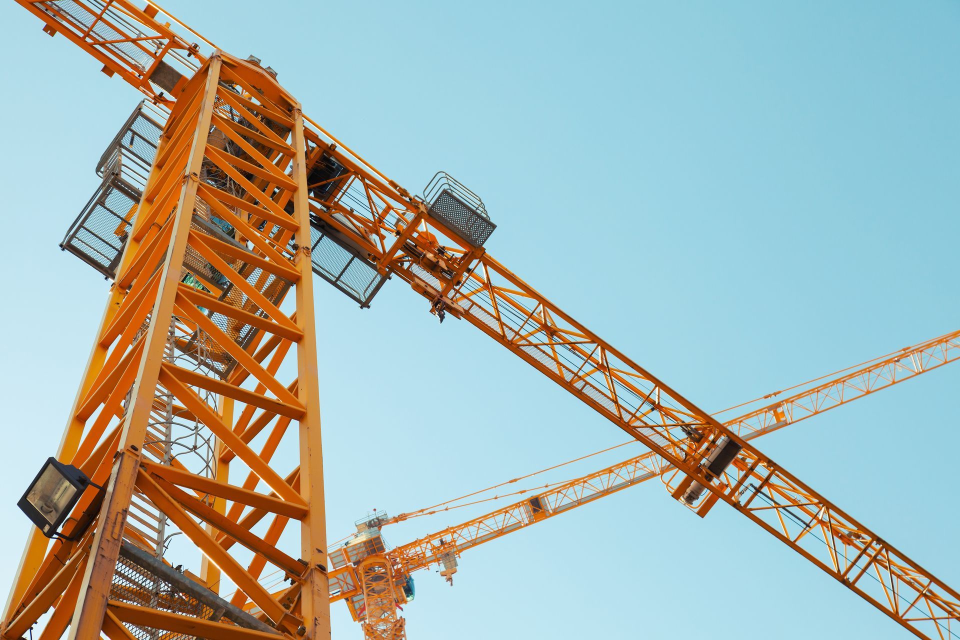 Orange construction cranes against a clear blue sky