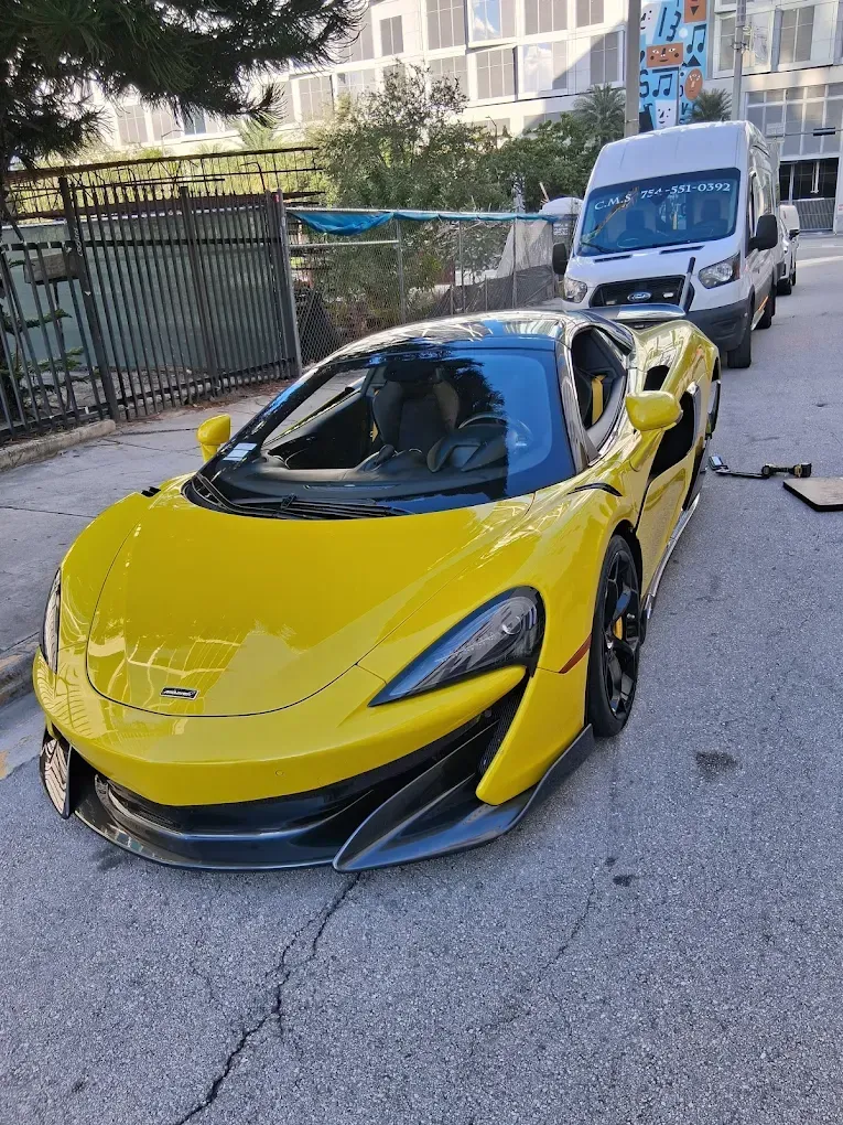 Yellow McLaren sports car parked on a street with a white van behind it.