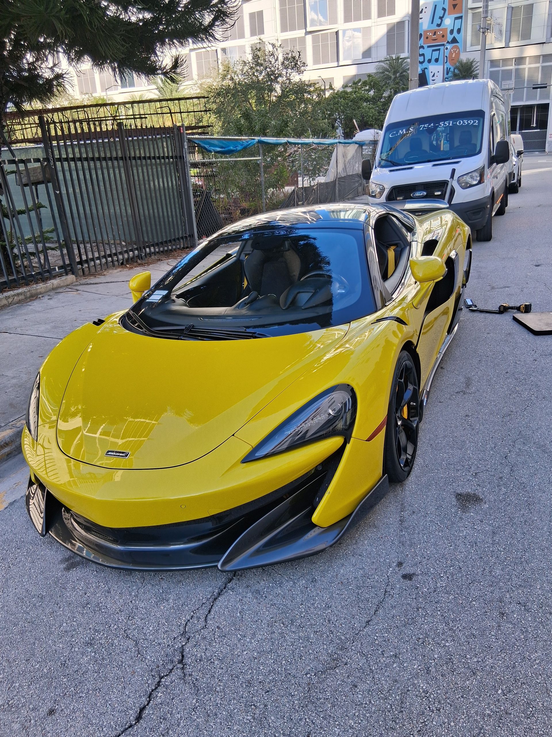 Yellow sports car parked on a street with a white van behind it.