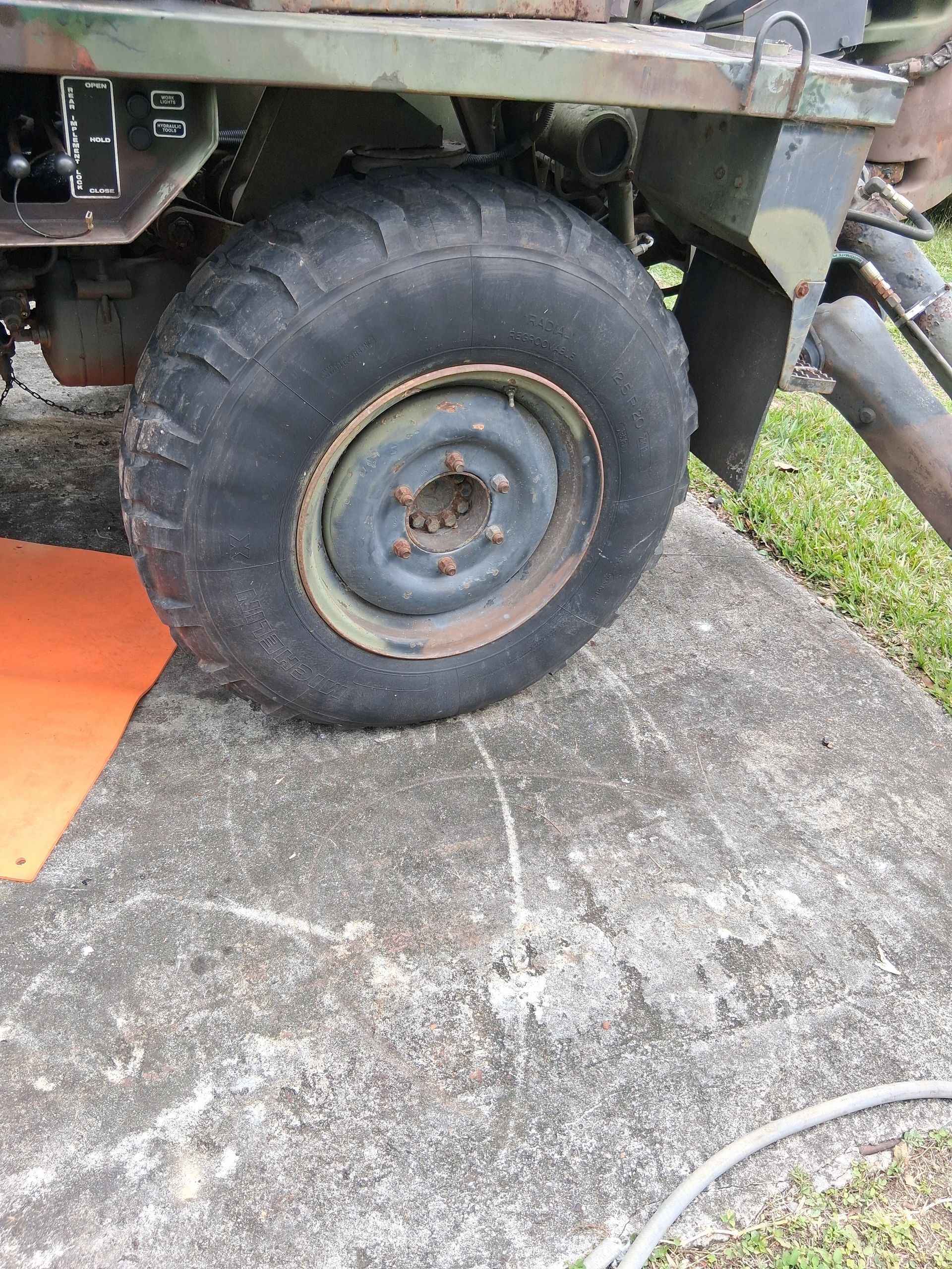 Close-up of a vehicle’s muddy tire on a concrete driveway beside grass and an orange mat.