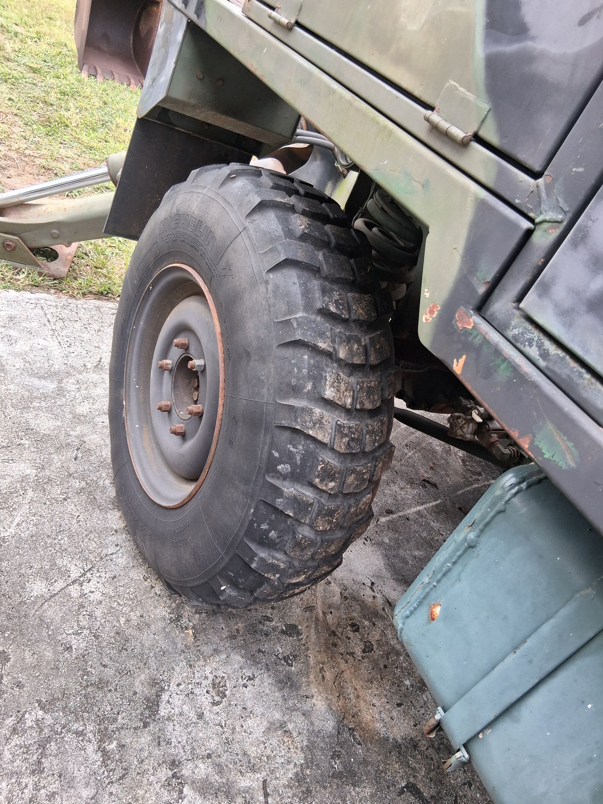 Close-up of a rugged off-road vehicle tire on gravel, with a green body panel above it.