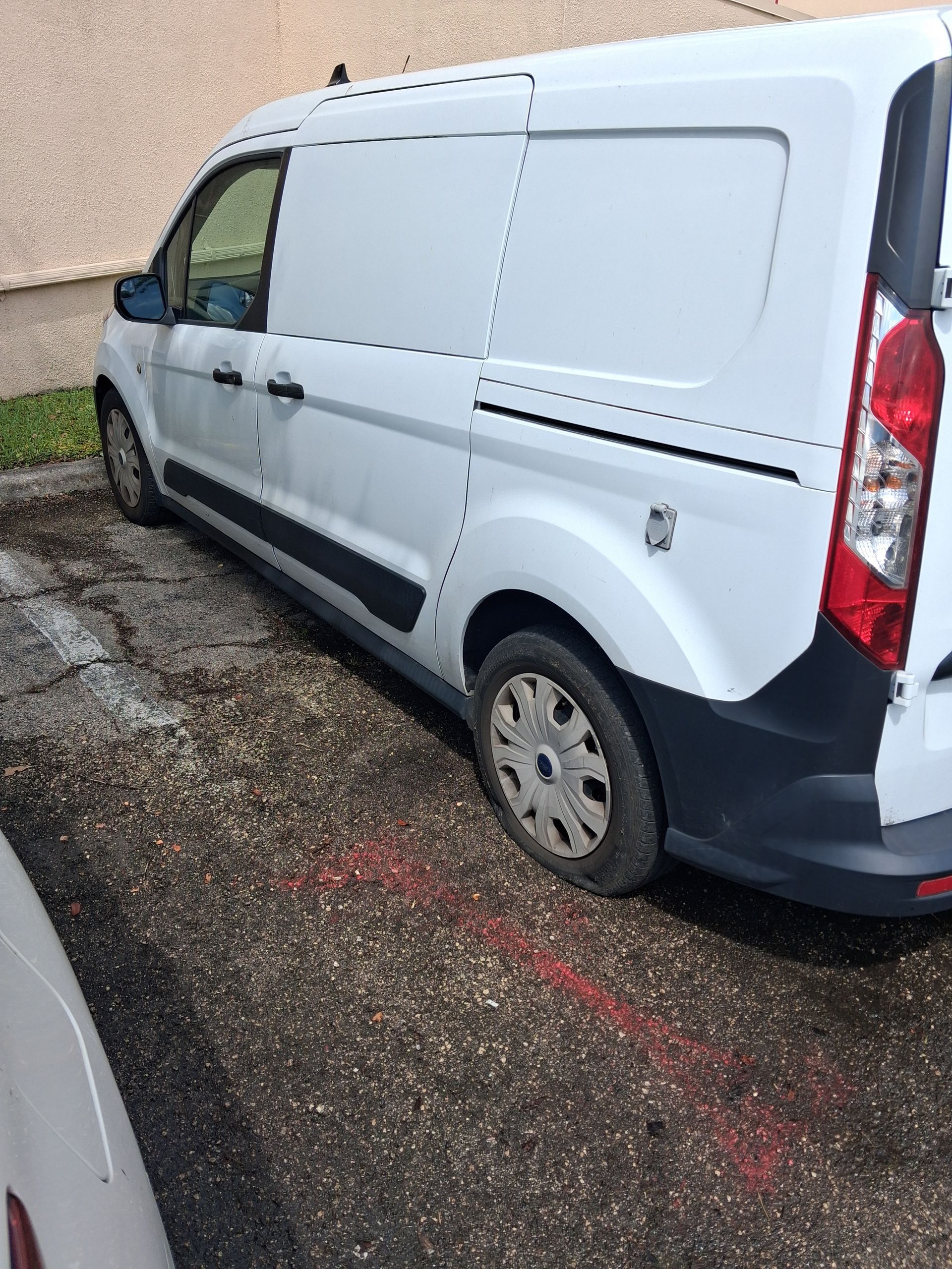 White cargo van parked on wet pavement beside a gravel lot, rear side view