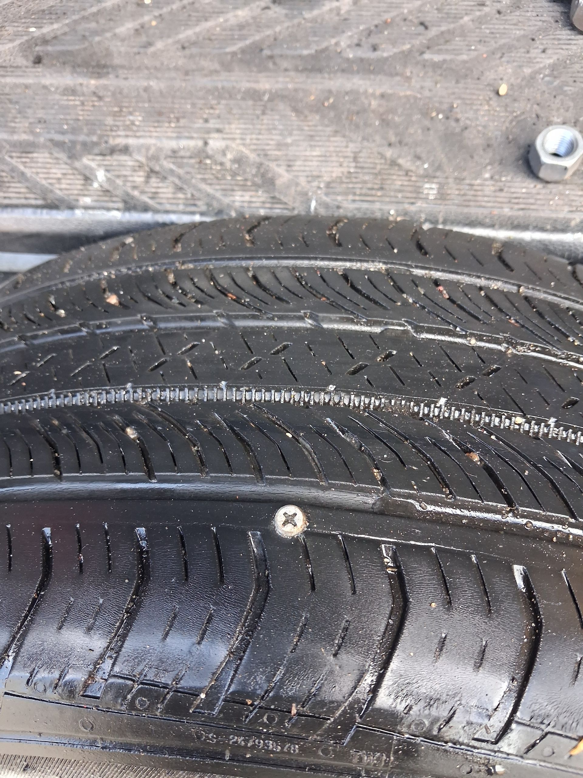 Close-up of a wet car tire tread on a wooden surface with a visible screw embedded in it