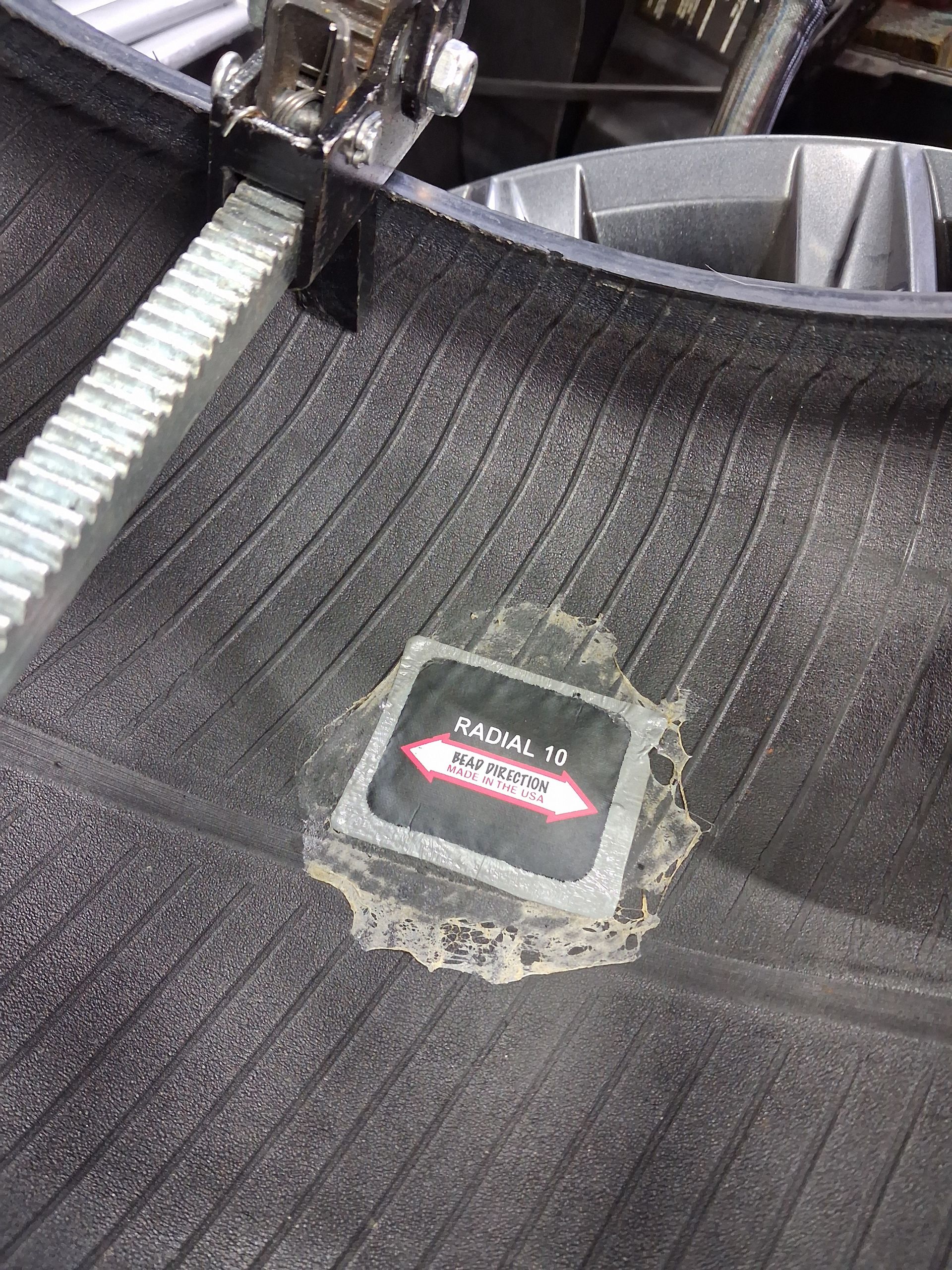 Dirty black carpeted floor mat with a small torn label near a car wheel well.