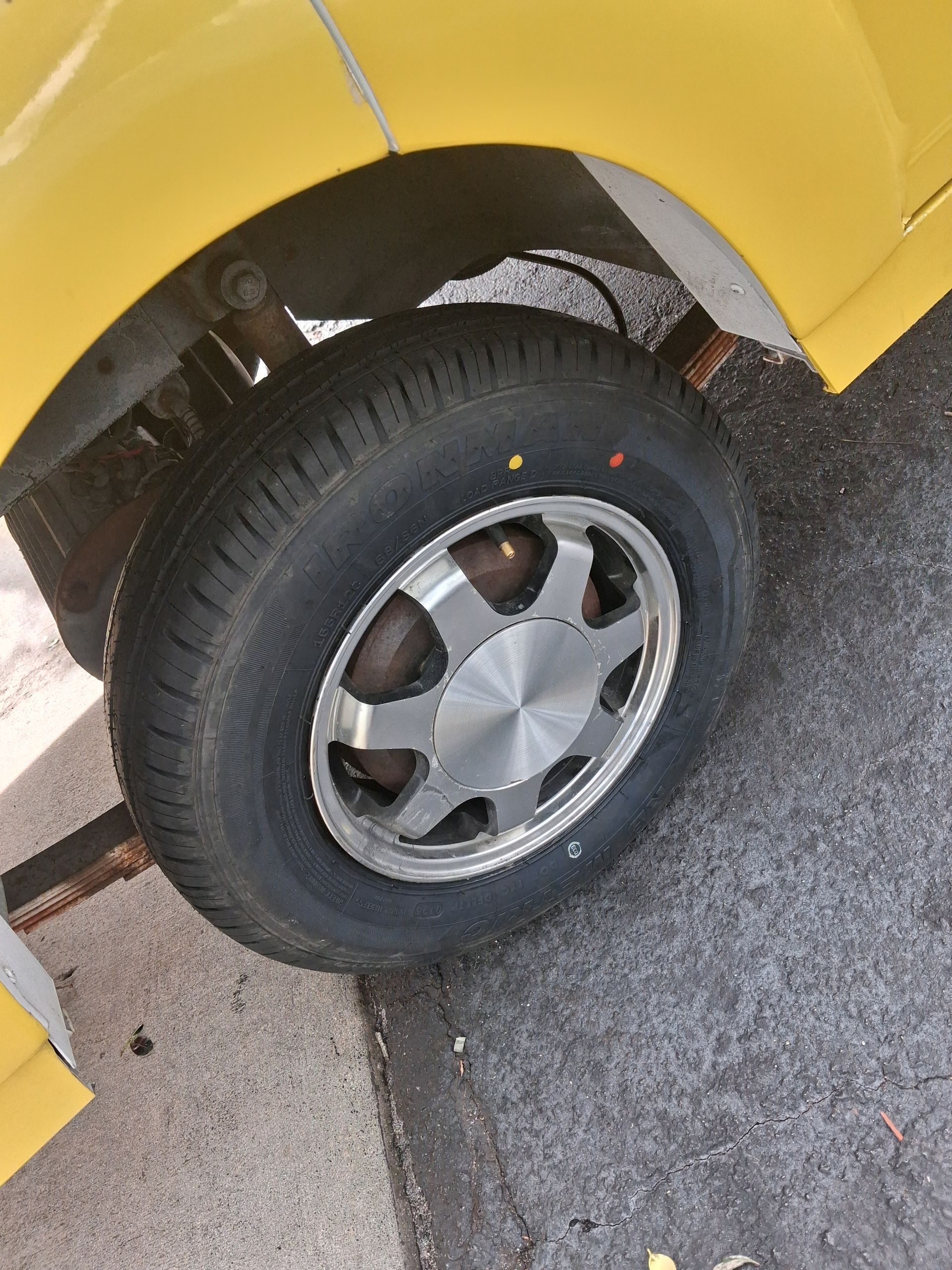 Close-up of a yellow vehicle’s front wheel and tire on cracked pavement, with a damaged fender edge.