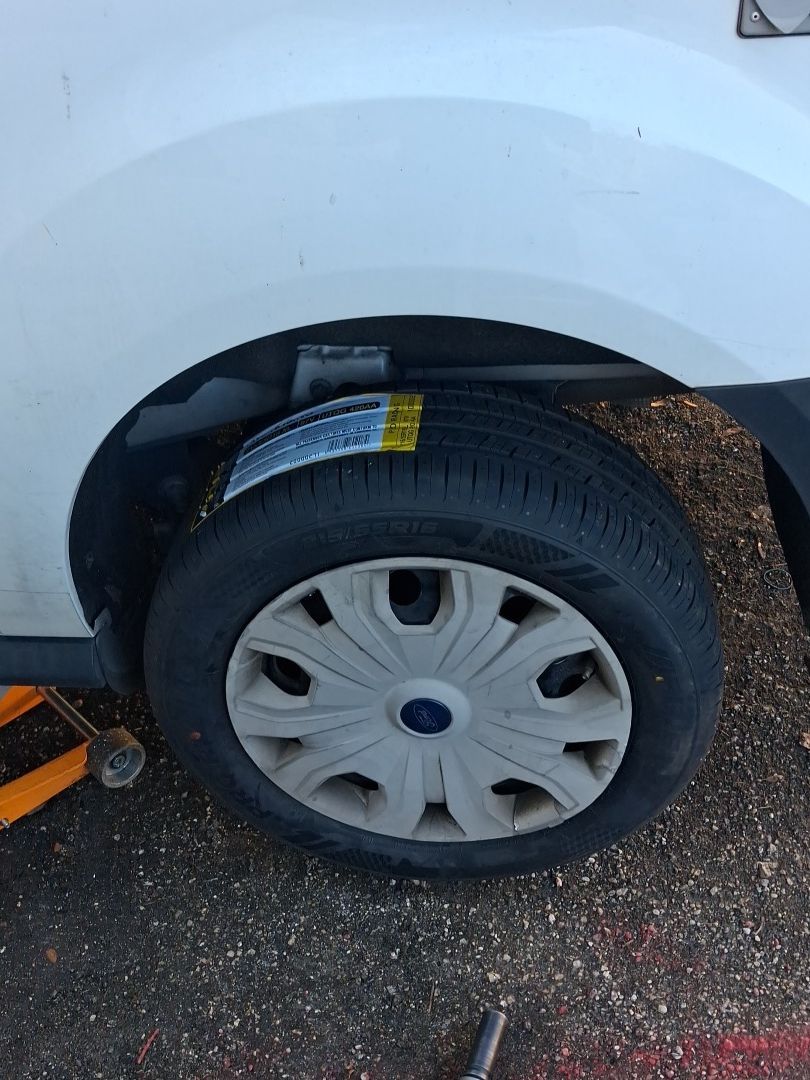 Close-up of a car wheel with a flat tire next to an orange jack on pavement