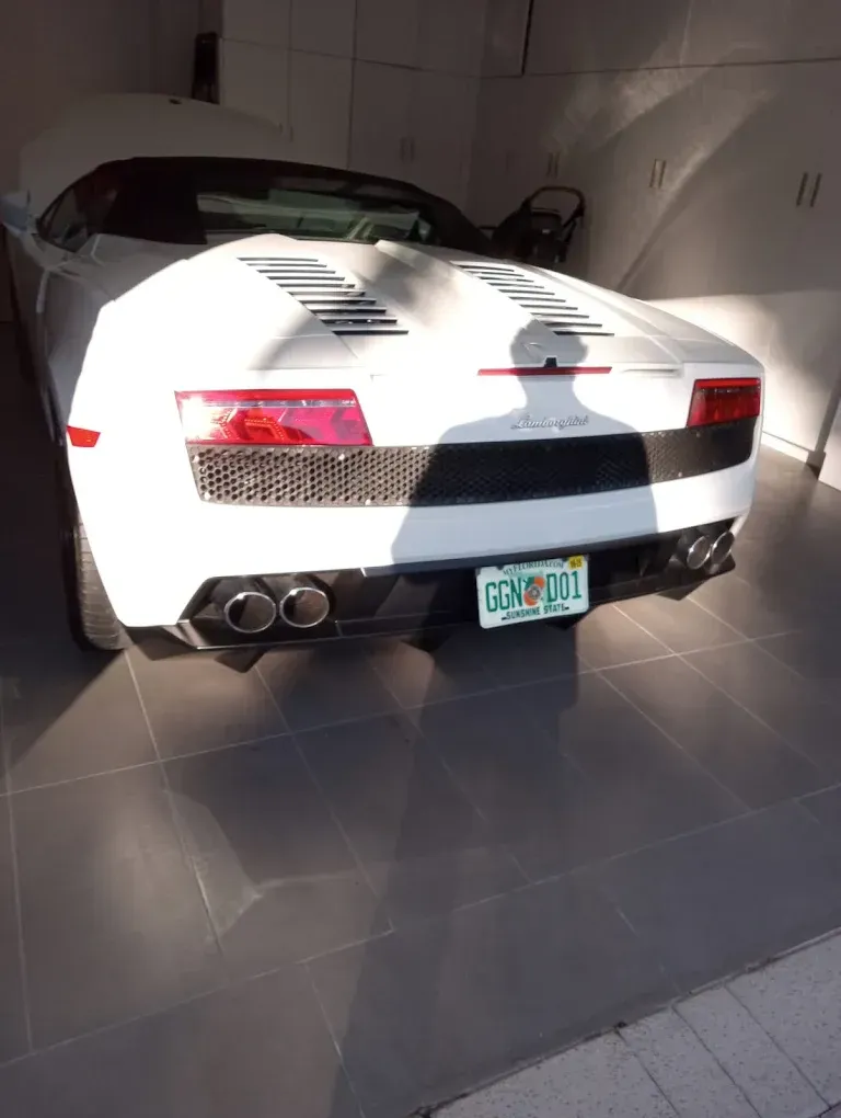 White sports car parked inside a garage, rear view with red taillights and a black racing stripe.