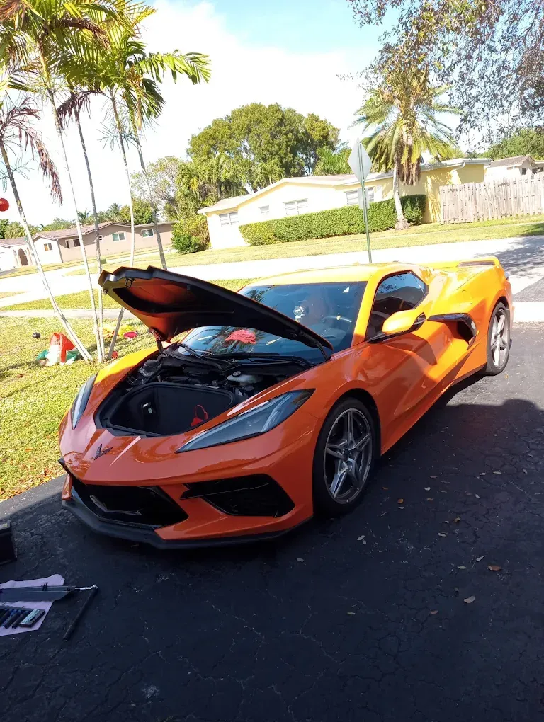 Orange sports car with hood open parked on a sunny street, with palm trees in the background