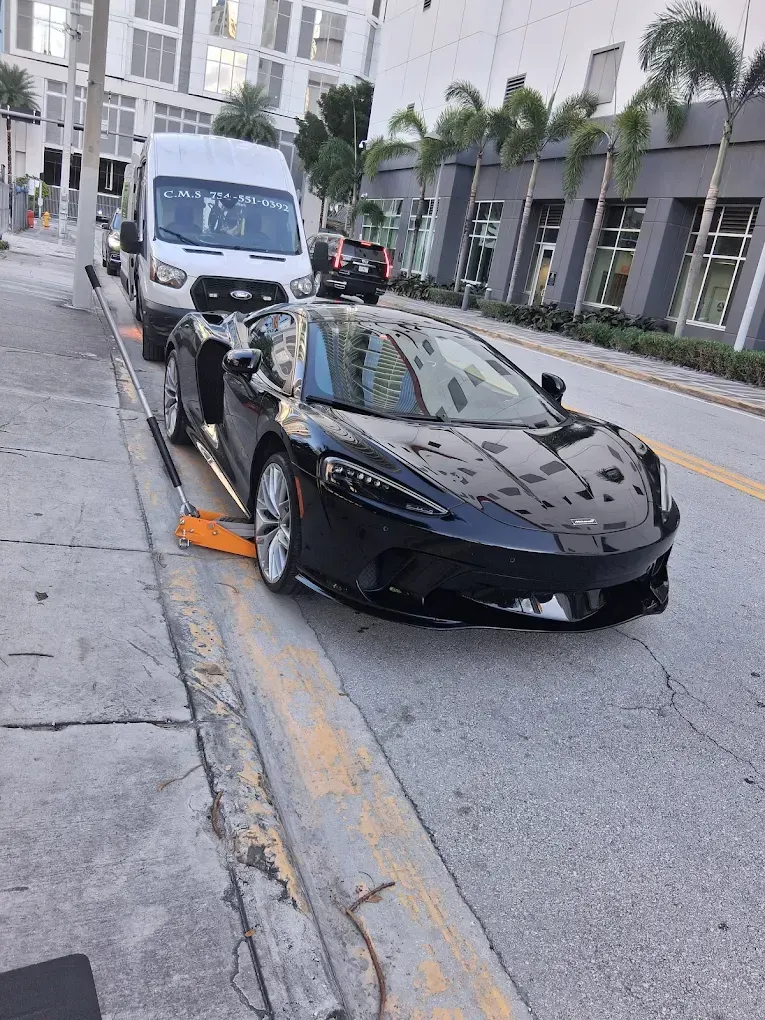 Gloved hands using a power drill to loosen lug nuts on a car wheel