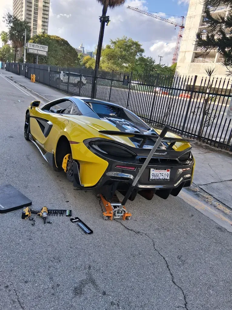 Yellow sports car on a city street, lifted by a jack with tools scattered nearby.