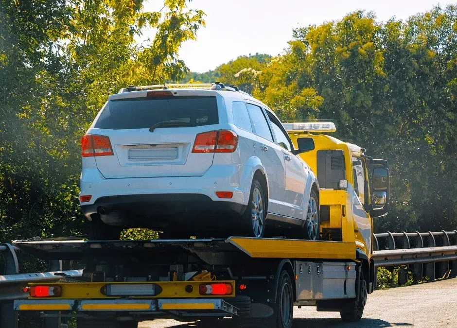 White SUV loaded on a yellow tow truck driving on a sunny road