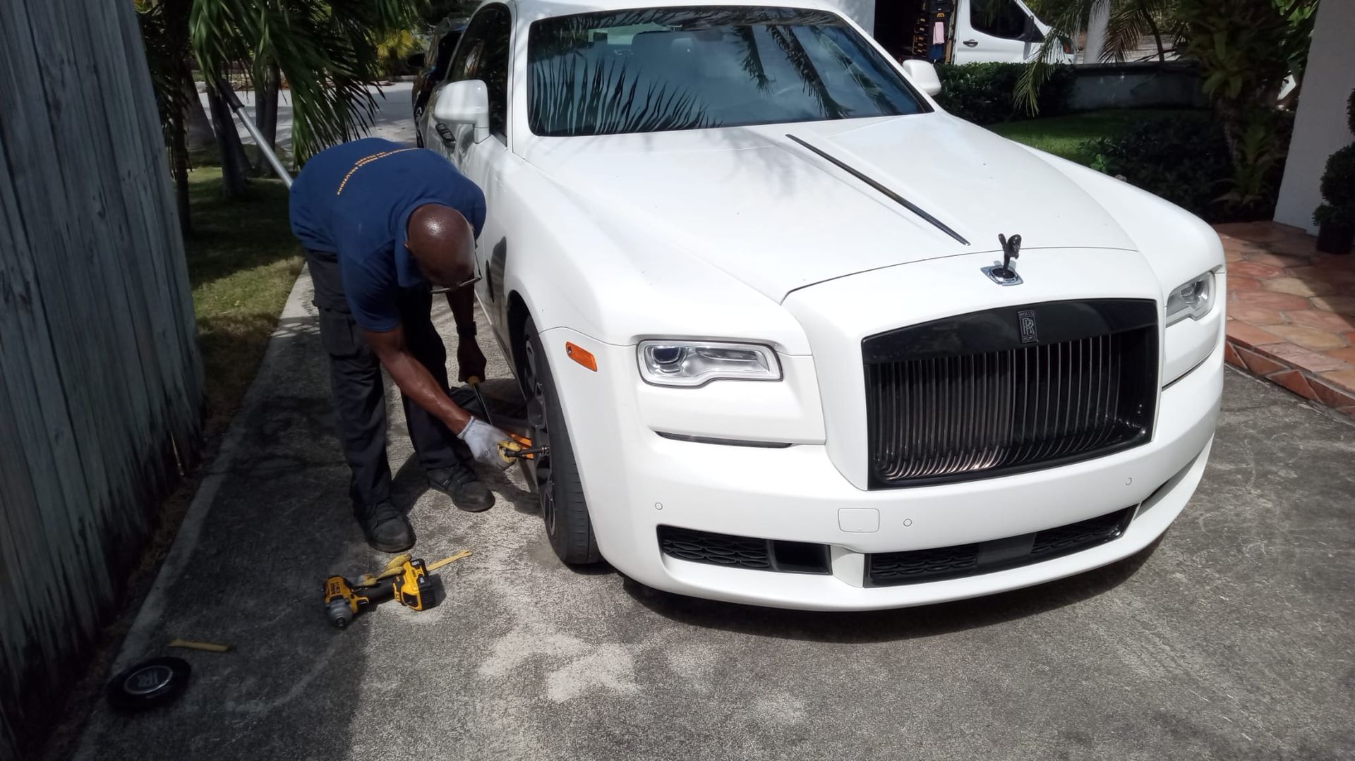 Mechanic changing a tire on a white luxury car parked outdoors
