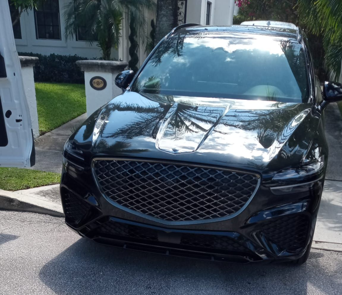 Black SUV parked by an open gate in a sunny driveway, front view with chrome grille.