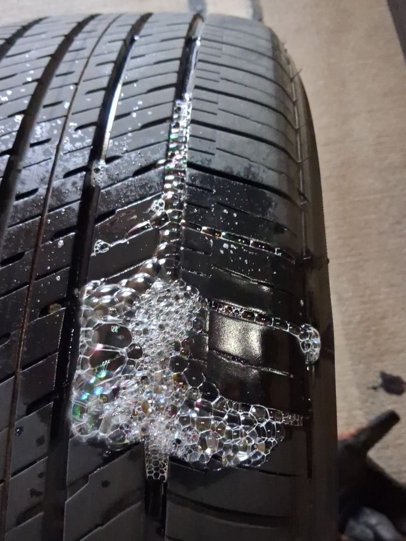 Close-up of a wet car tire with soap suds and a damaged tread section.
