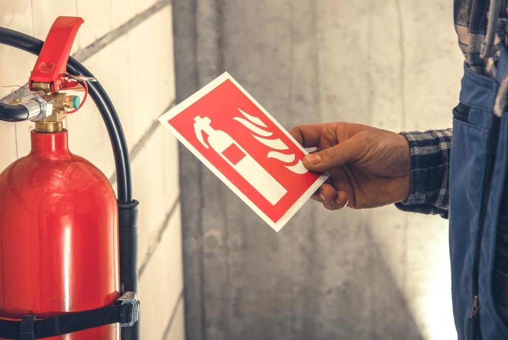A Man Is Holding a Fire Extinguisher Sign in Front of A Fire Extinguisher — Stellar Test and Tag in Armidale, NSW