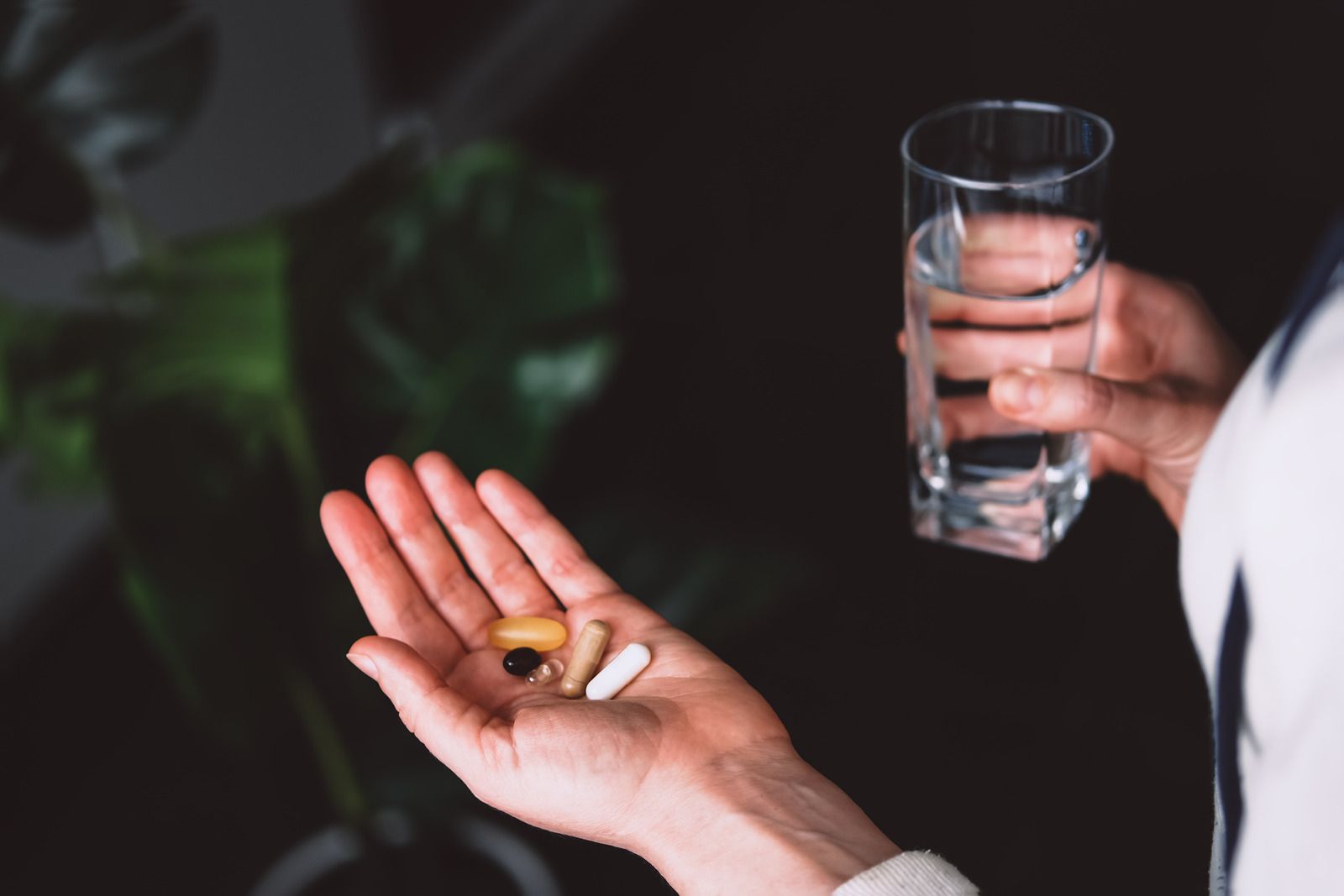 A person is holding a glass of water and a handful of pills.