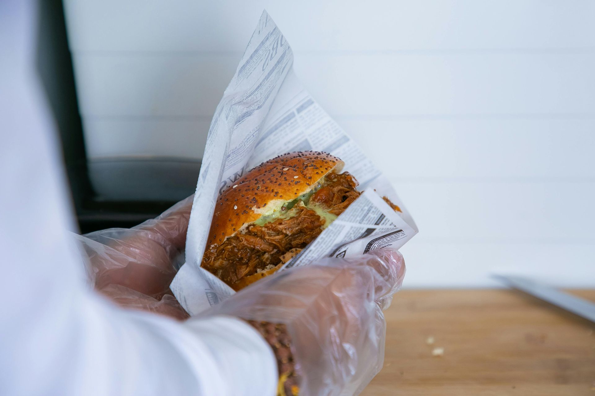 A person wearing plastic gloves is holding a hamburger wrapped in paper.
