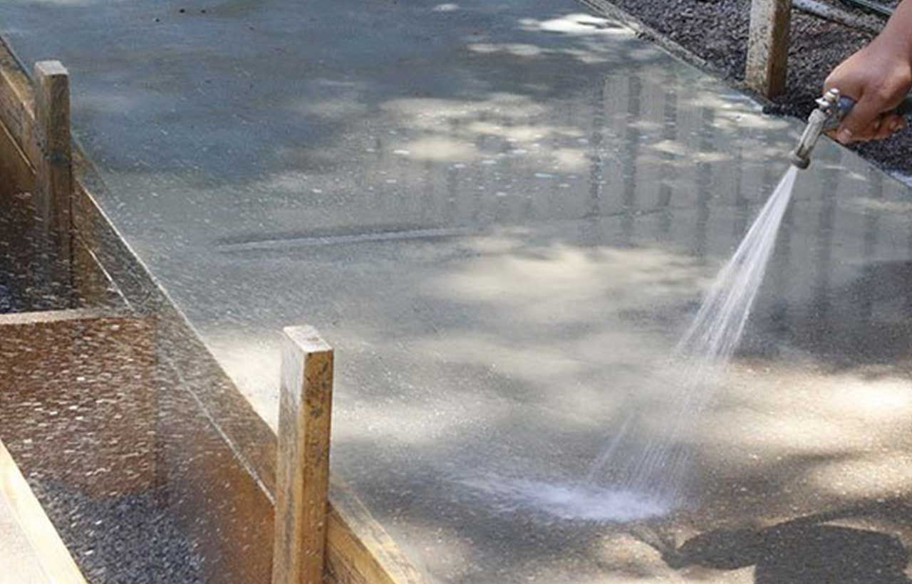 A person is using a hose to curing a concrete surface.