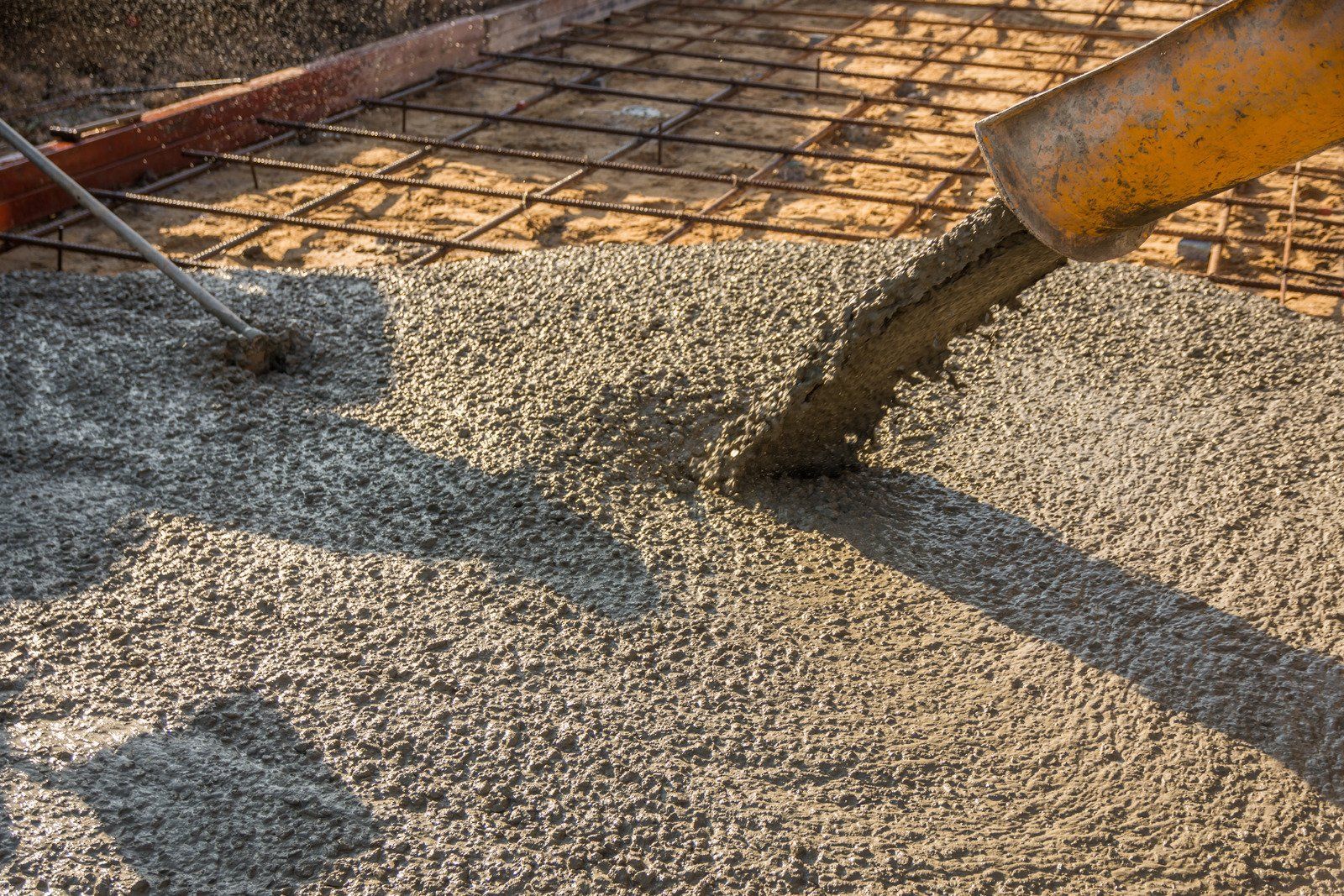 Concrete being poured from a chute onto a steel mesh, construction site.