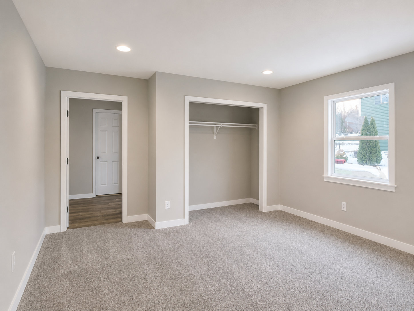 Empty carpeted bedroom with two open closets, a doorway, and a window letting in daylight.
