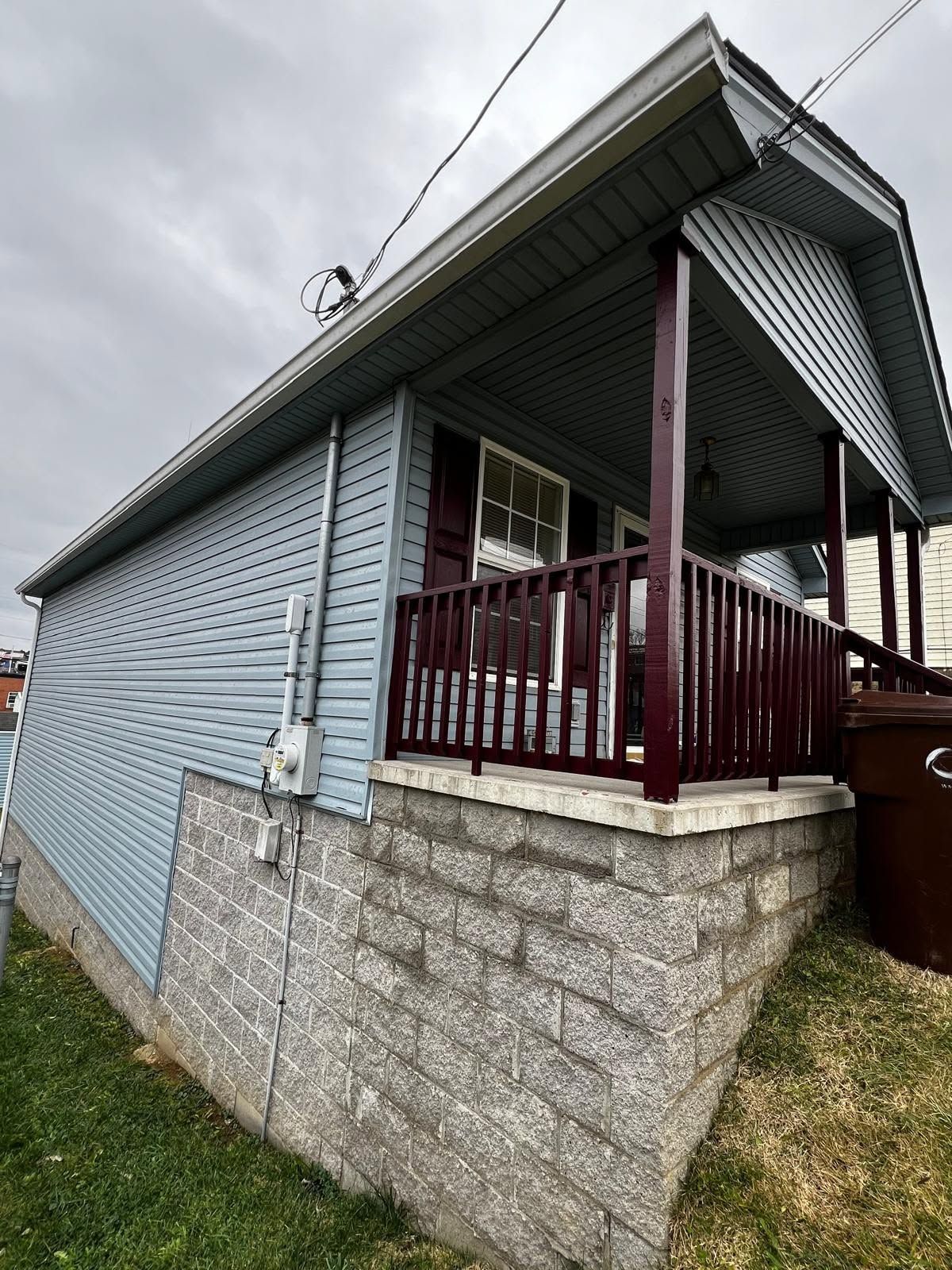 Small blue house with a maroon porch on a stone foundation, viewed from the side.
