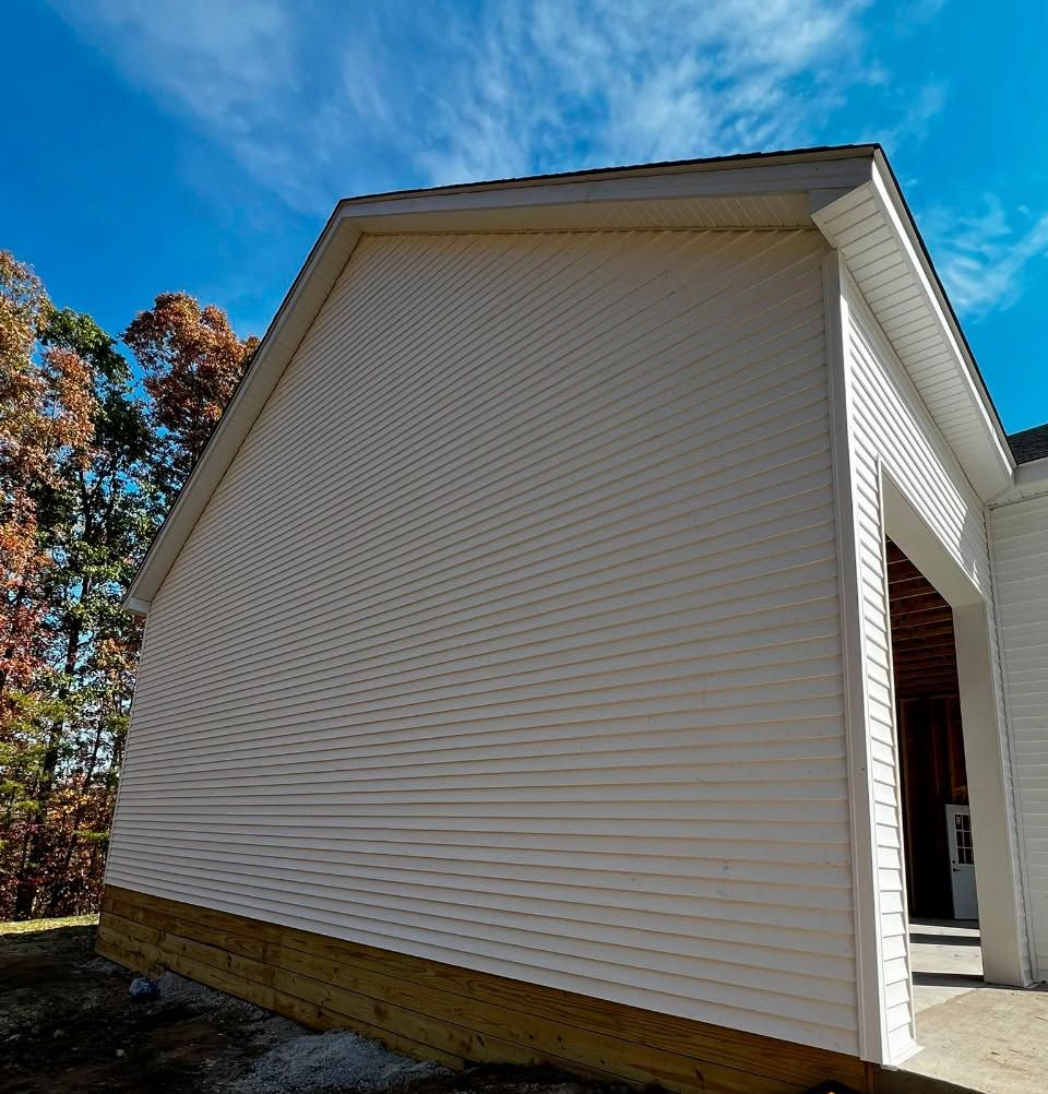 White vinyl-sided house exterior with a gabled roof and a covered entryway, viewed from below under a blue sky