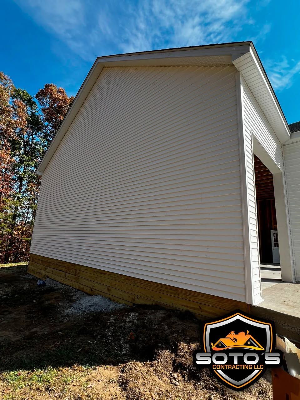 White-sided house with a tan foundation and open garage entry under a blue sky
