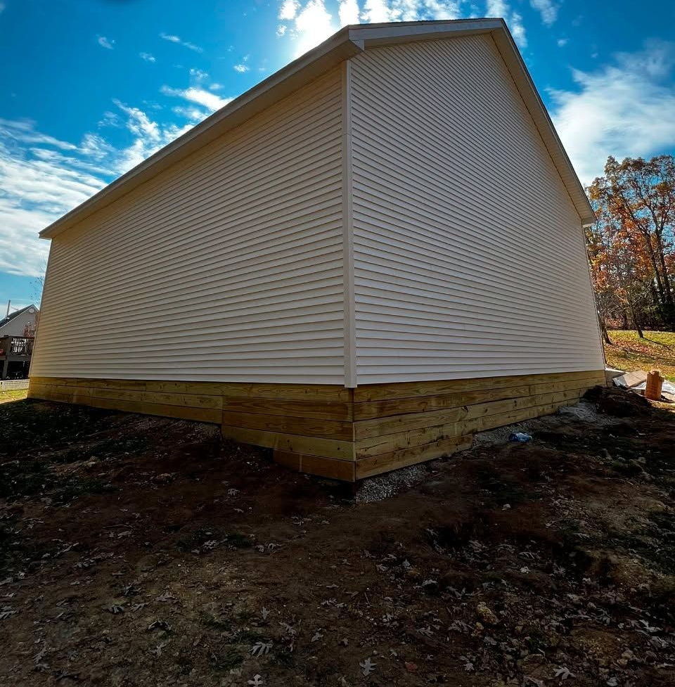 White vinyl-sided building with a gabled roof on a bare lot under a blue sky