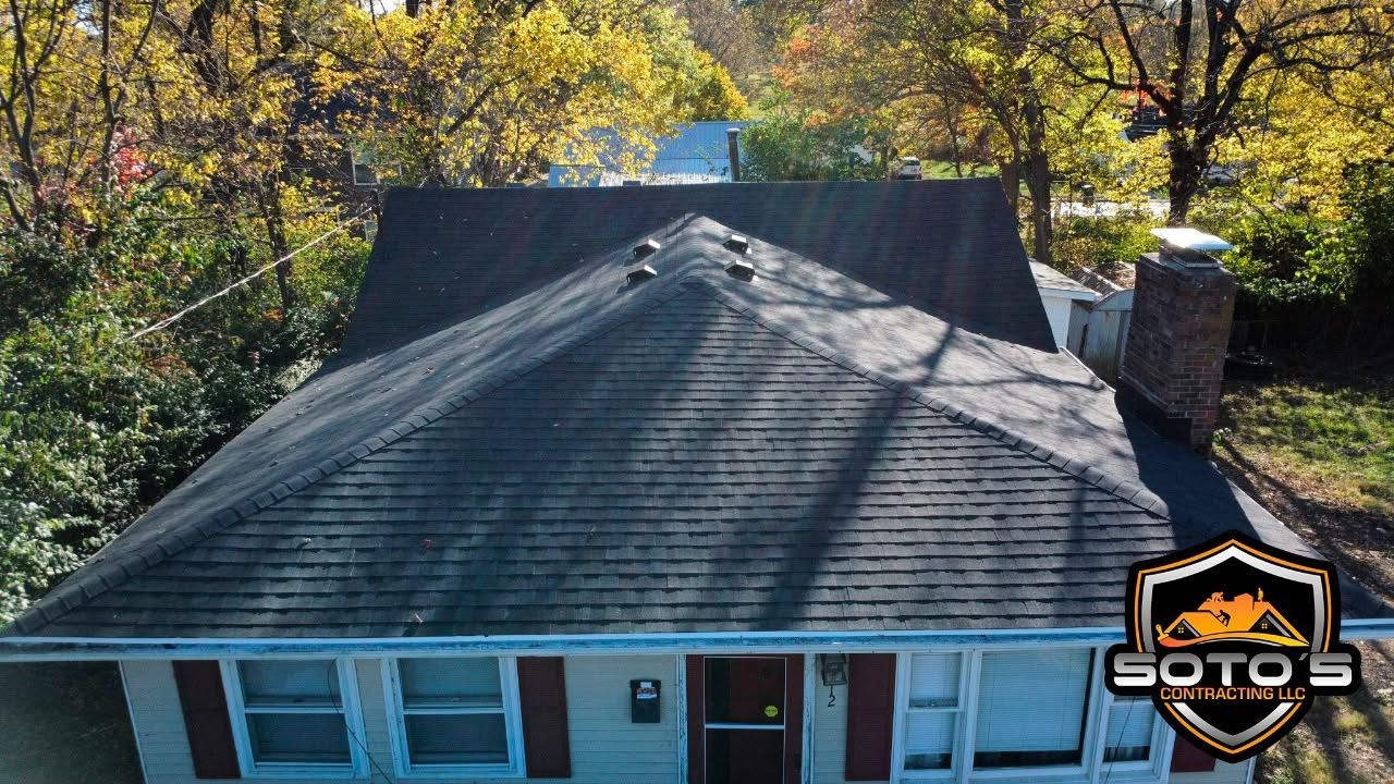 Aerial view of a house roof with a chimney, surrounded by autumn trees.
