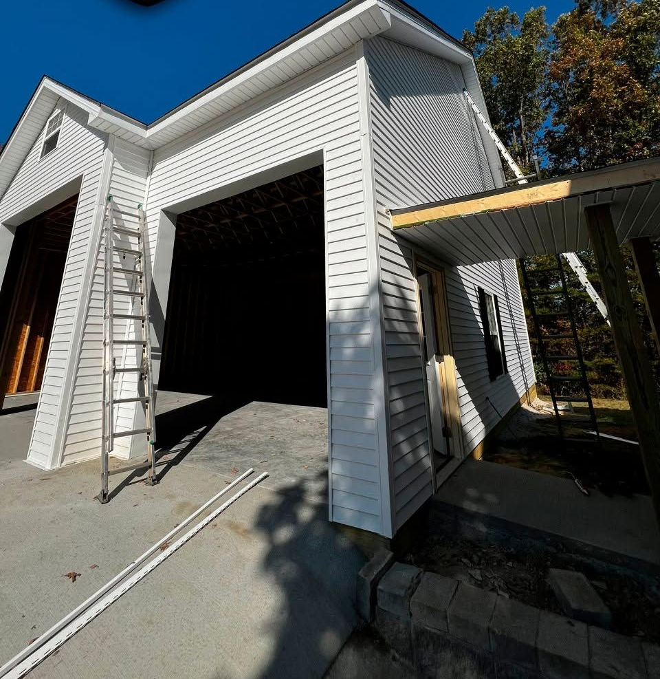 White house exterior with an open garage, ladder on the driveway, and a covered side walkway