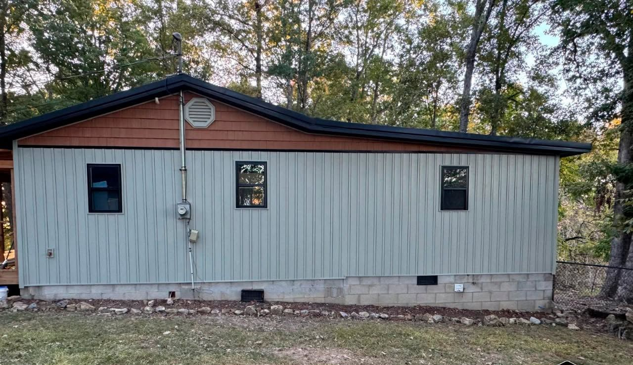 Small gray metal building with a dark roof, three windows, and trees in the background