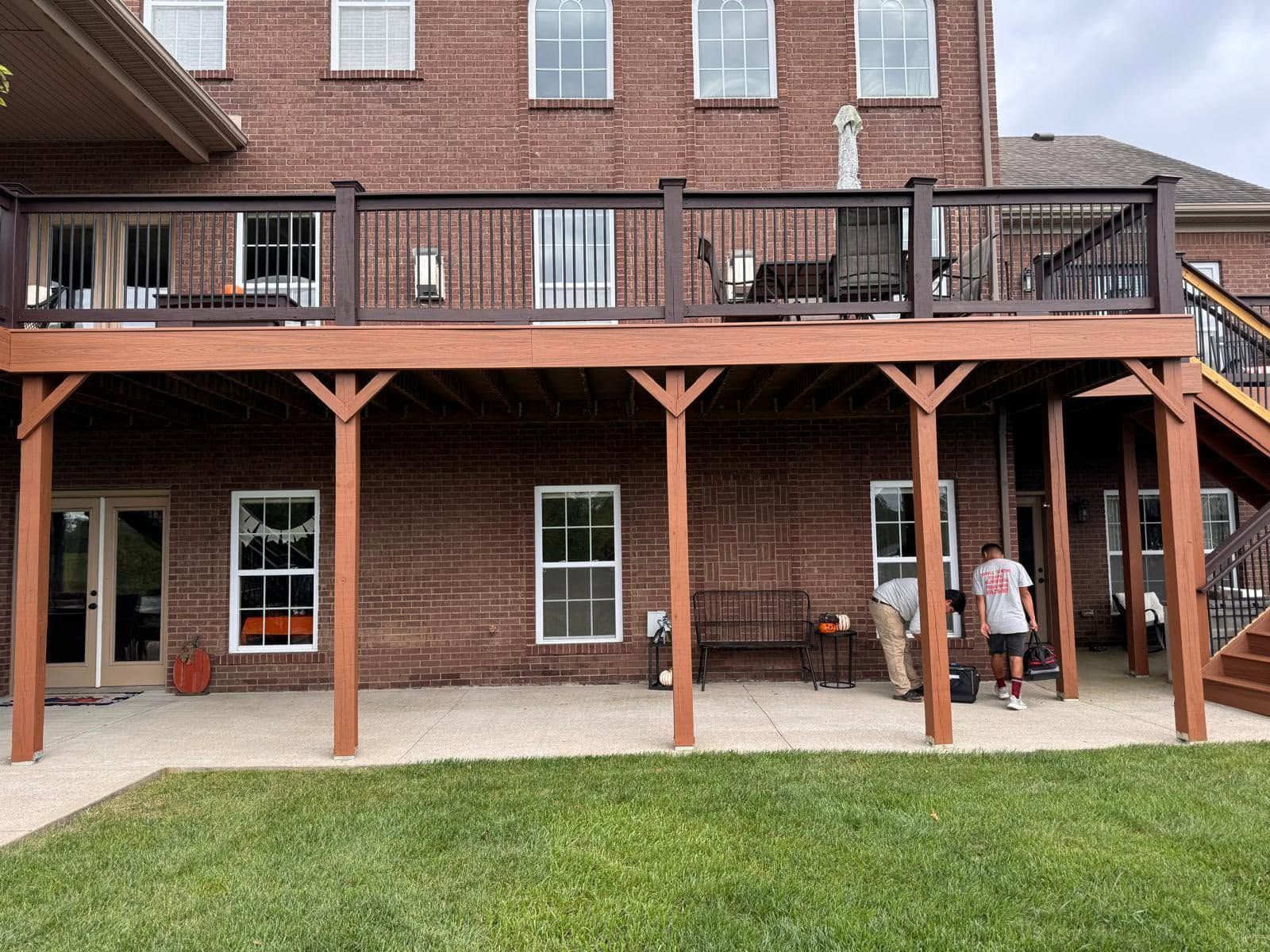 Brick house with a raised wooden deck and two people standing on the back patio.